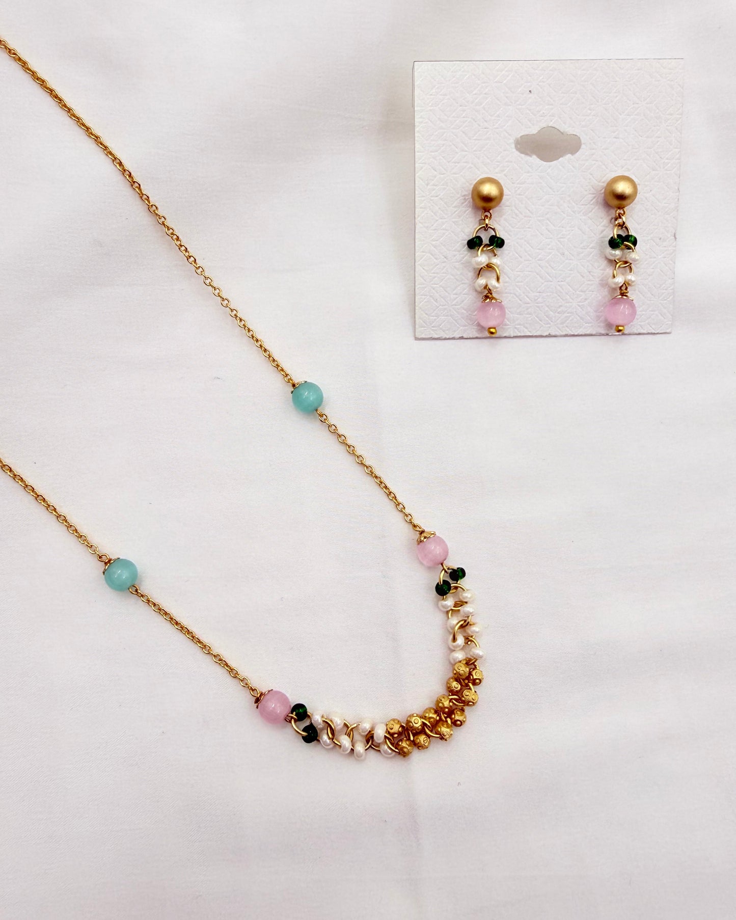 A gold-tone necklace and matching stud earrings set with pastel beads, displayed on a white background. The necklace features a gold chain with a curved section of gold beads, white pearls, and pink, green, and light blue beads.
