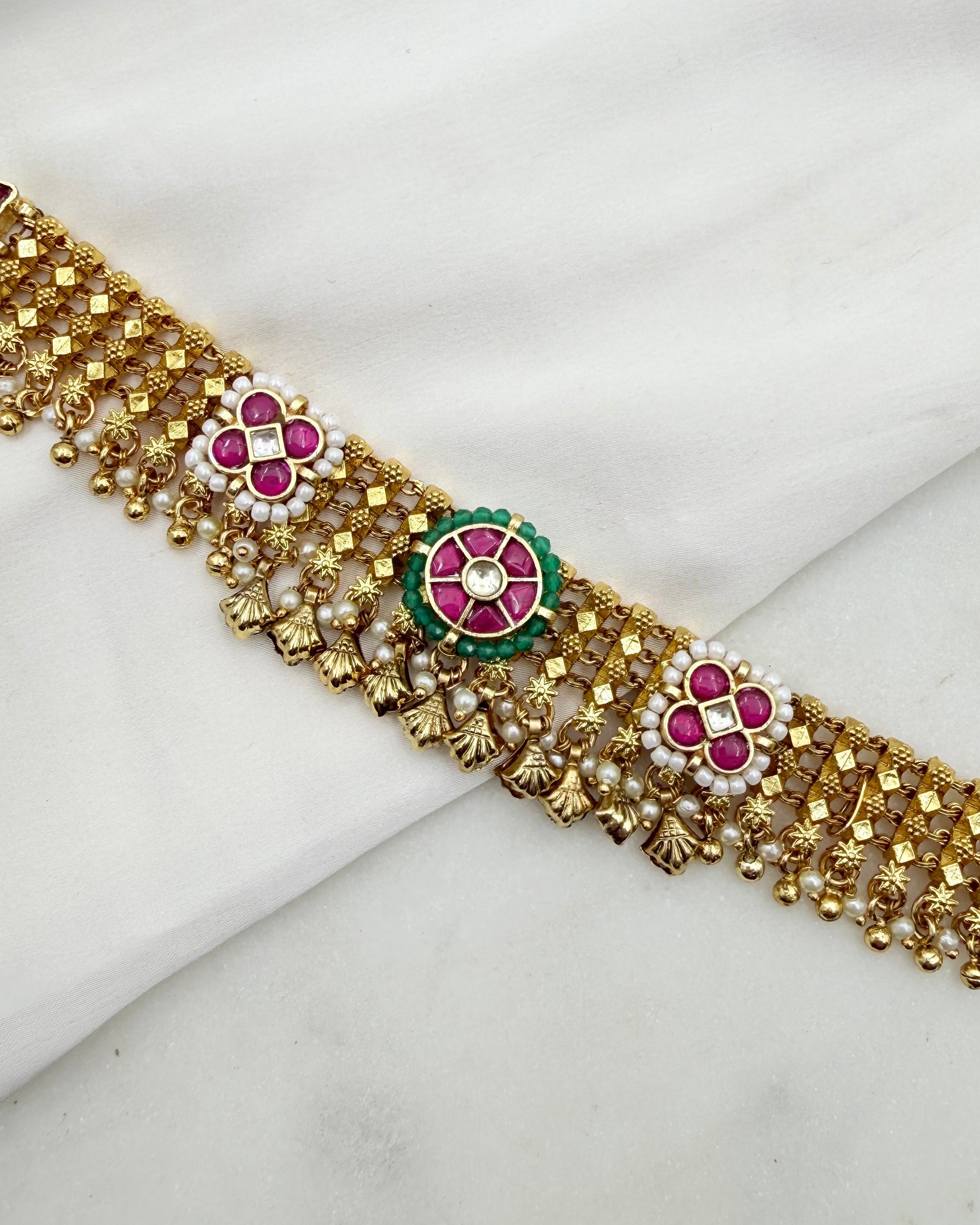 Gold-toned traditional Indian choker necklace with red floral motifs, white stones, and green accents, displayed on a white fabric background.
