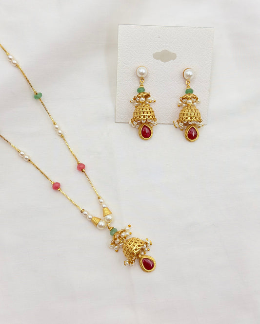 Gold-toned jewelry set featuring a necklace and matching earrings with pearl-like white beads, small green accents, and red teardrop stones, displayed on a white background with a card.