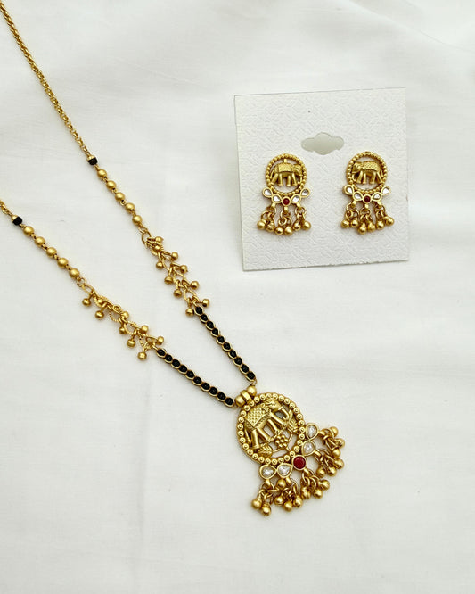 Gold-toned traditional jewelry set featuring a necklace with a detailed pendant and matching stud earrings, displayed on a white fabric background with the earrings on a small card.
