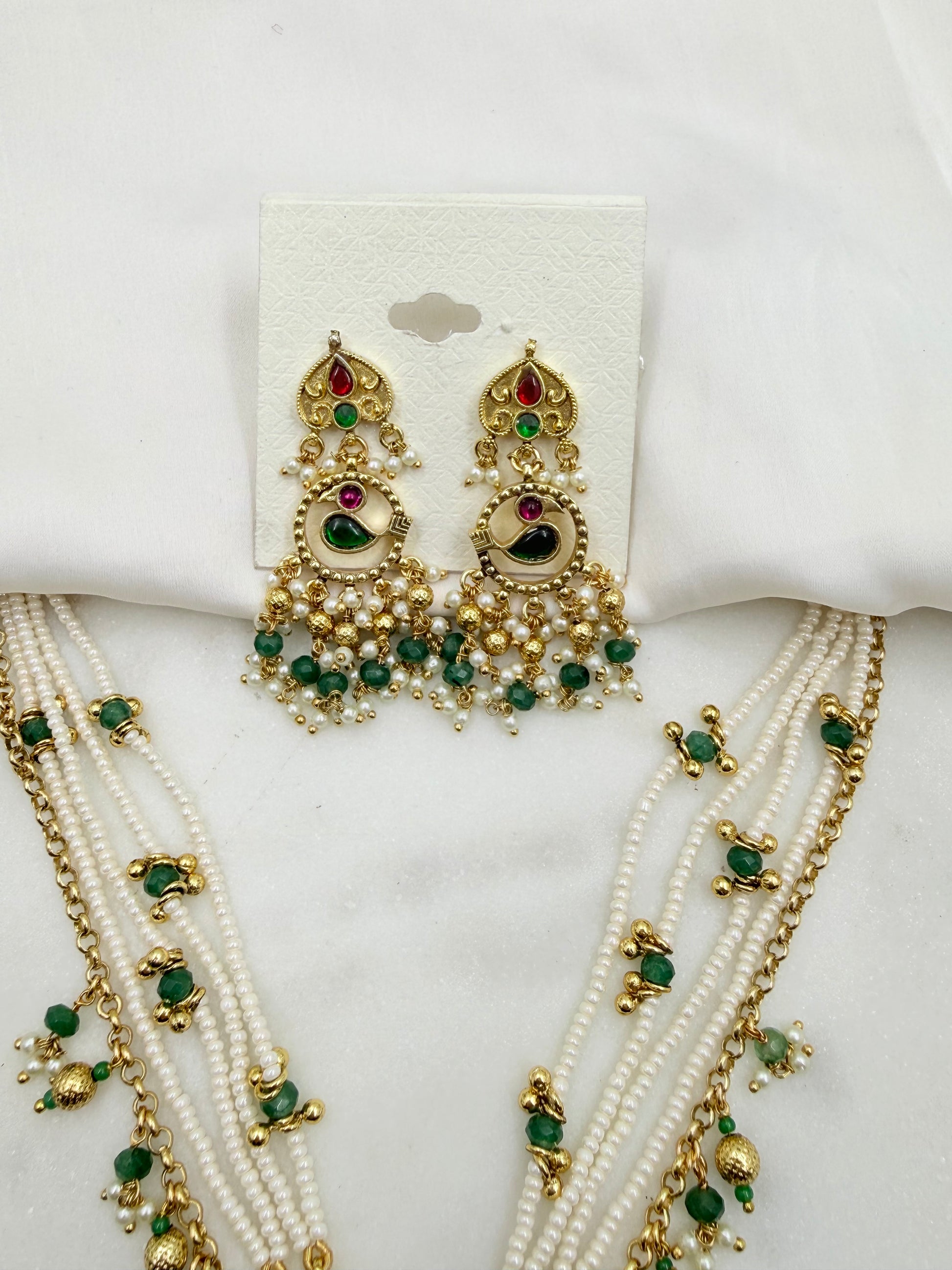 Gold and white beaded jewelry set featuring a pair of dangling earrings on a white display card and matching multi-strand necklaces draped below, decorated with green and red stones.