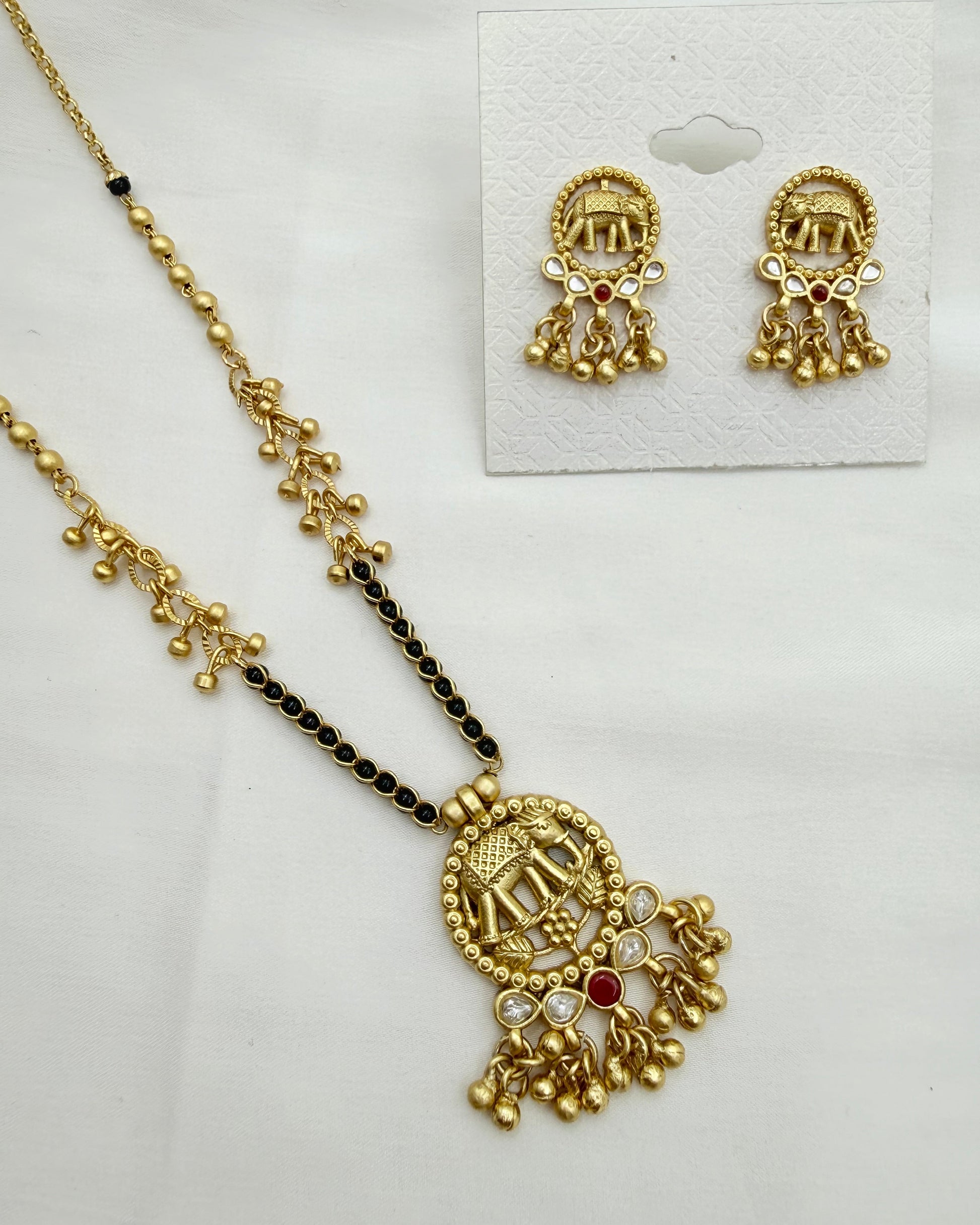 Gold-toned traditional jewelry set featuring a necklace with a detailed pendant and matching stud earrings, displayed on a white background with a small card holding the earrings.
