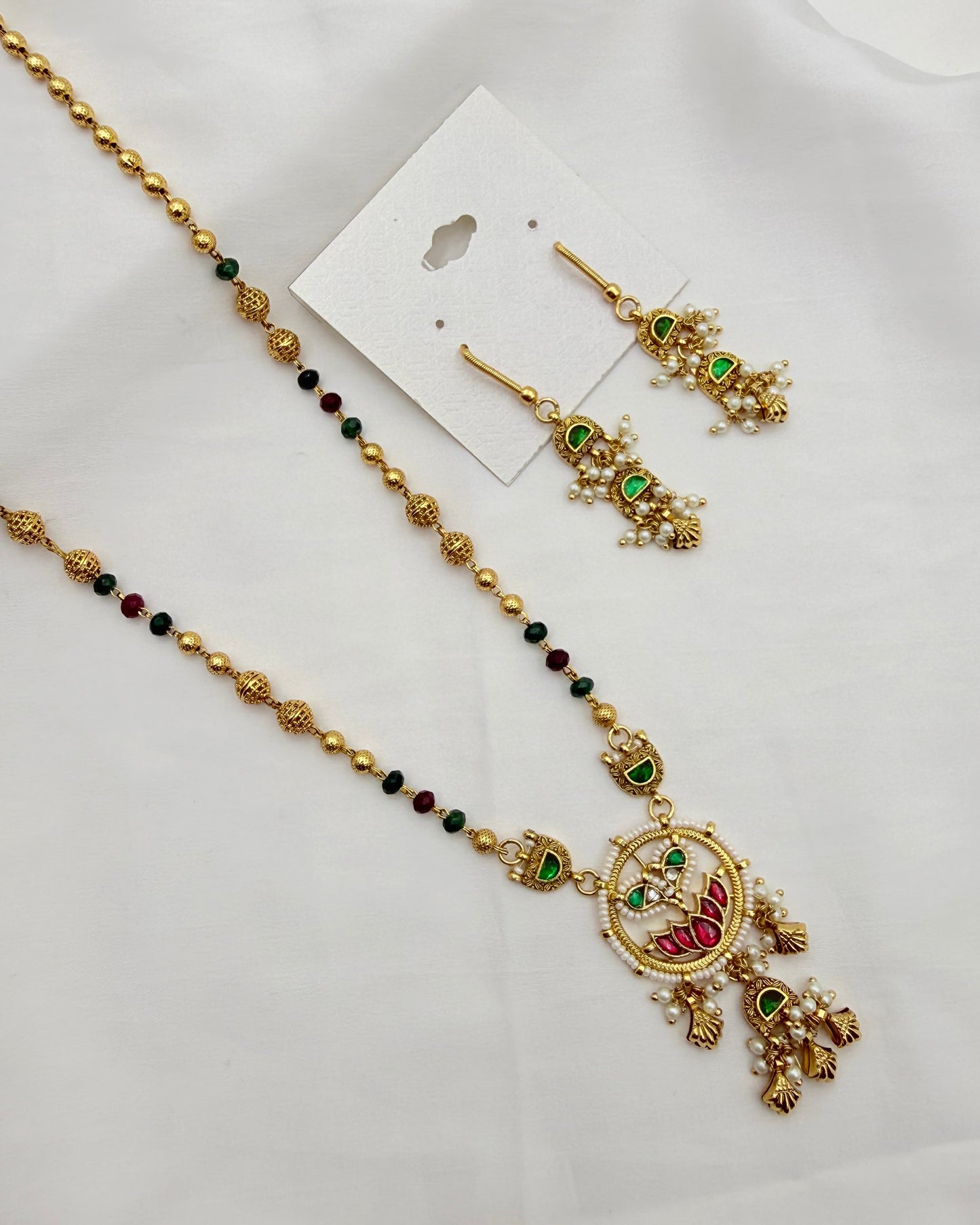 Gold-toned traditional jewelry set including a necklace with a decorative pendant, matching drop earrings, and a white display card on a white fabric background.