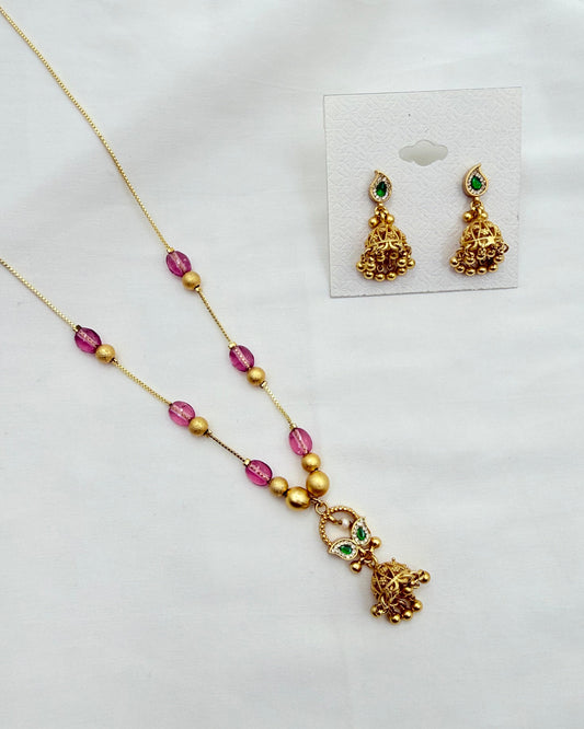 Gold-toned jewelry set featuring a necklace and matching earrings with pink faceted beads, gold spacer beads, and small green stone accents, displayed on a white surface with the earrings shown on a small card.