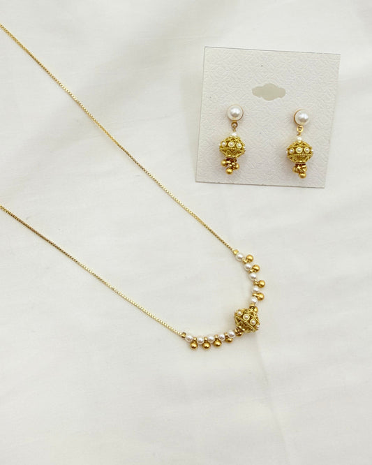 Gold jewelry set featuring a delicate chain necklace and matching stud earrings with pearl-like studs and textured gold drops, displayed on a white fabric background with a small card backing.