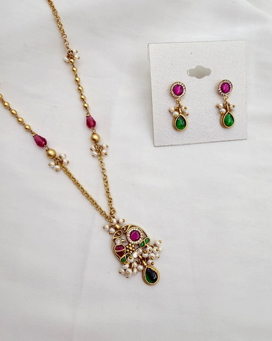 Gold-plated Indian style jewelry set featuring a necklace and matching earrings with pink and green stones and white pearl accents, displayed on a white background with the earrings on a card.