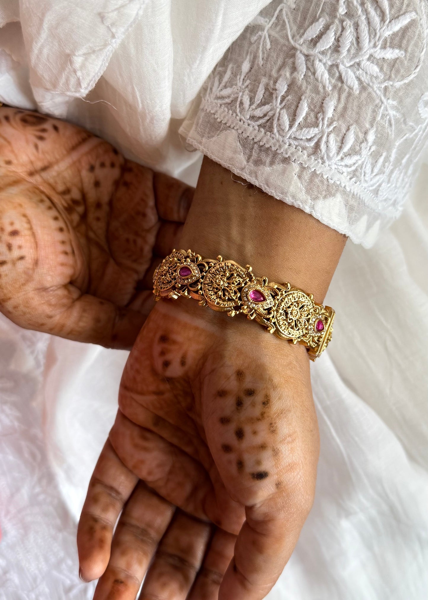 Close-up of a hand wearing a gold bracelet with pink stones on a white fabric background