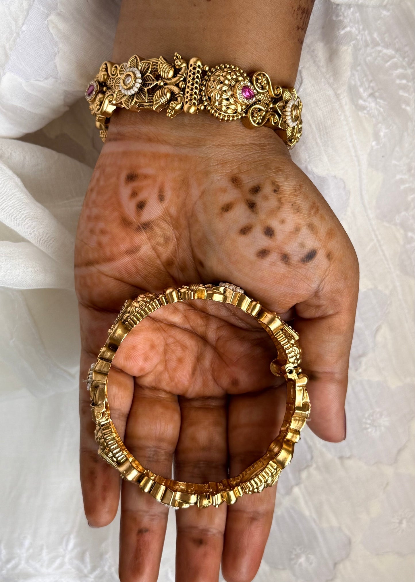 Hand wearing gold bracelets with a white lace garment in the background